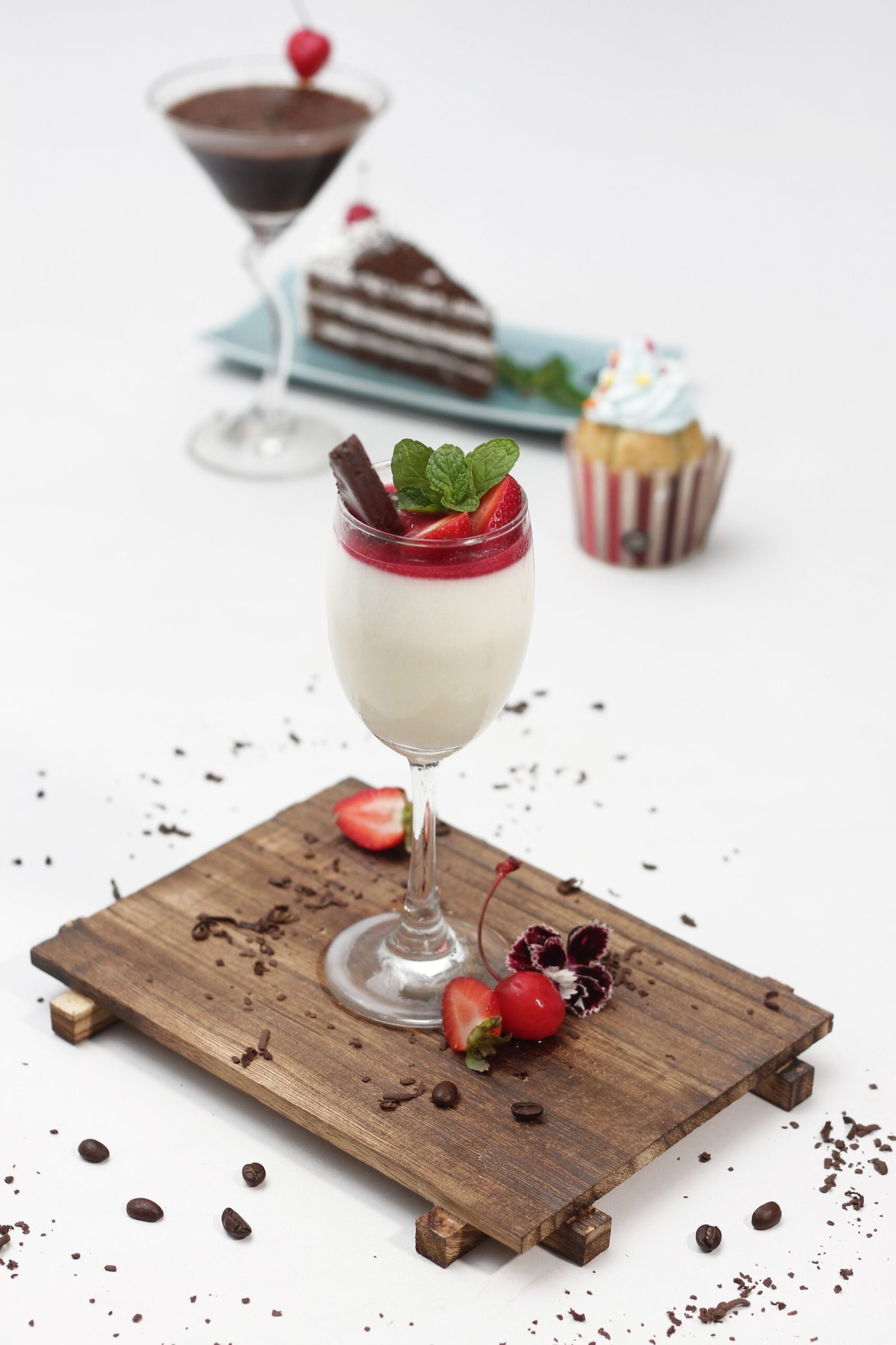 Strawberry panna cotta topped with berry sauce, fresh strawberries, mint, and a chocolate wafer in a glass.