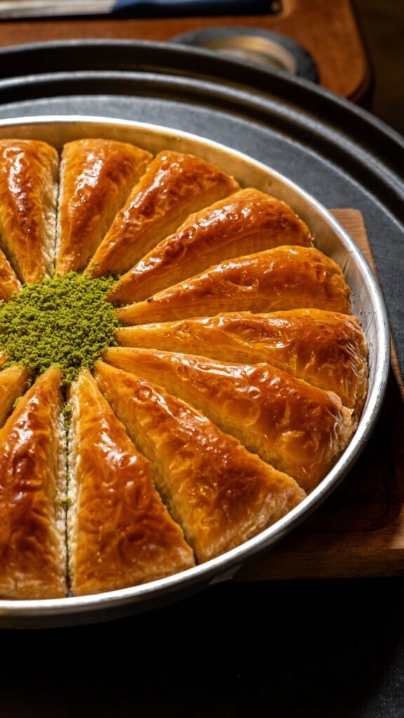 Pistachio Baklava: A Crisp, Buttery Dessert Made for Sharing Golden pistachio baklava slices arranged in a round tray with finely ground pistachios in the center.