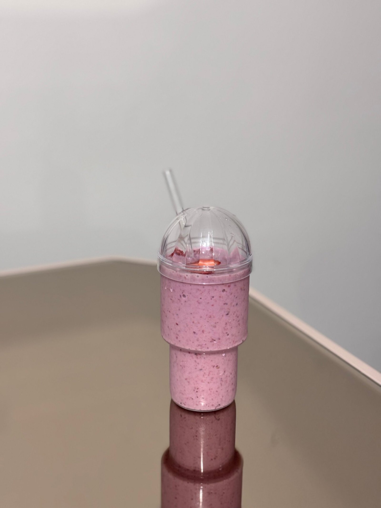 Easy Strawberry Smoothie Recipe for a Fresh and Creamy Drink Single strawberry smoothie in a clear takeaway cup with dome lid and straw on a reflective table